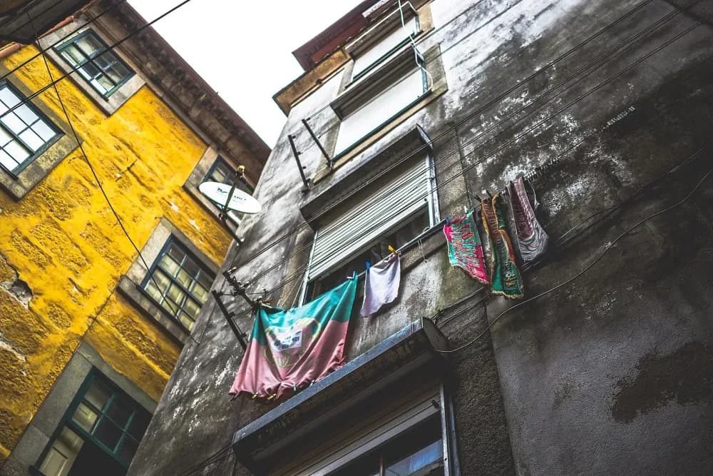 Narrow city street looking up at rustic buildings with a Portuguese flag and laundry hanging out.